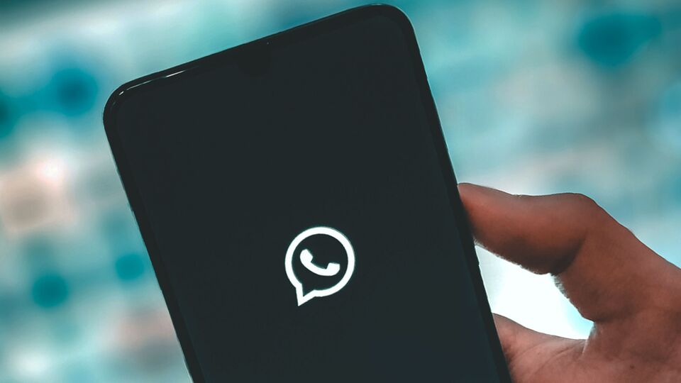 A close-up image of a hand holding a smartphone, which shows a WhatsApp logo