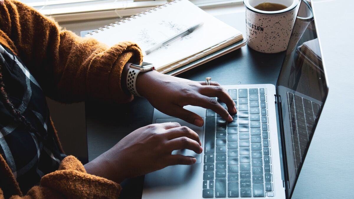 Hands typing on a laptop, notepad and cup nearby