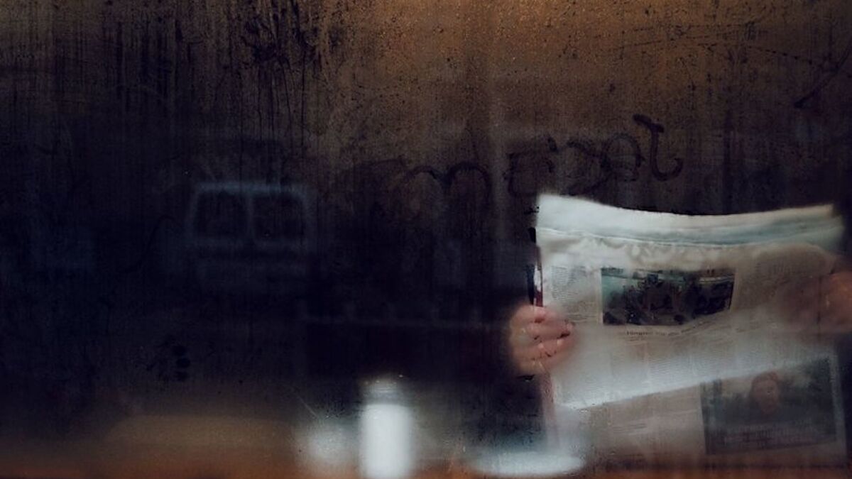 A newspaper, held up, behind a window covered in condensation