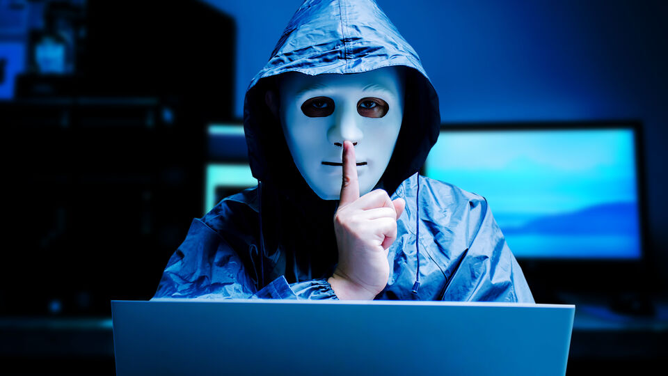 Hooded character raises a finger to the lips of a masked face