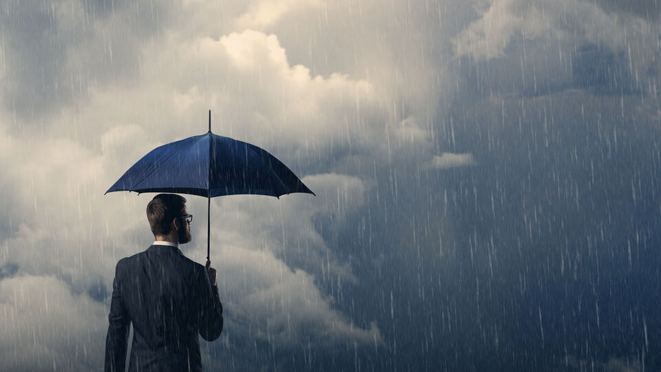 Surrounded by rain and angry clouds, a suited fellow stands under an umbrella