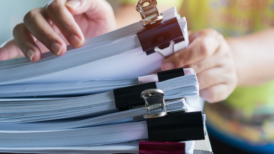 Hands sifting through wads of paper held together by bulldog clips