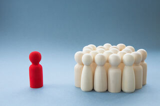 Red wooden figure standing next to a group of white wooden figures