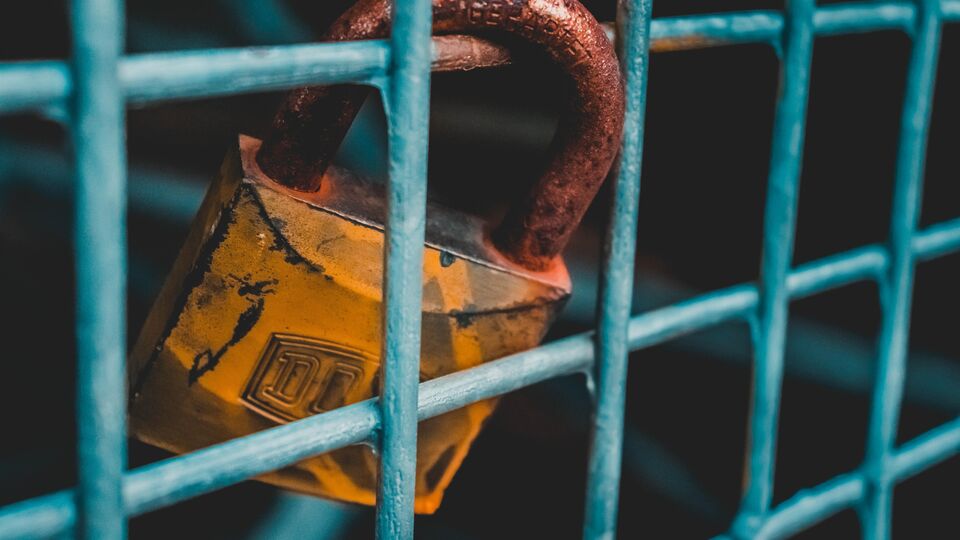Rusty padlock attached to metal fence